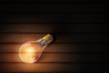 Light bulb on wooden surface Glowing glass light bulb on wooden background