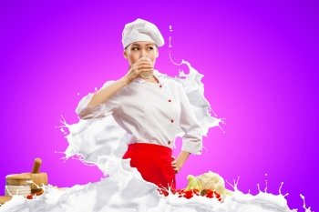 Asian female cook against milk splashes Asian female cook against milk splashes in red apron against color background drinking milk