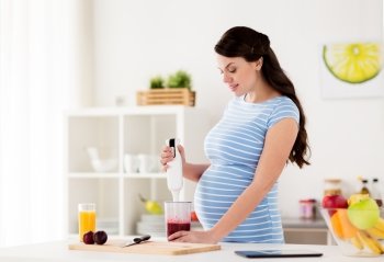 healthy eating  cooking  pregnancy and people concept - pregnant woman with blender preparing fruit smoothie drink at home kitchen pregnant woman wit