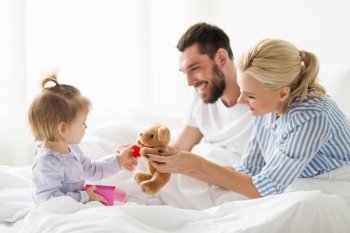 people  family  holidays and morning concept - happy little girl and parents with gift box in bed at home happy family with gift box in bed at home