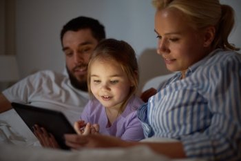 people  family and technology concept - happy mother  father and little girl with tablet pc computer in bed at night home happy family with tablet pc