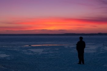 man watching the sunset on the shore of the winter lake