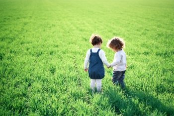 Two children going in spring green field