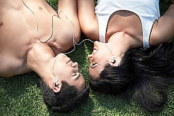 Couple listening to mp3 player lying down on grass view from above