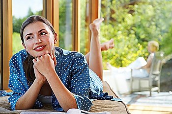 Woman with hands clasped to chin lying on front near windows overlooking forest