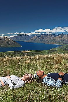 Man and woman lying in field overlooking hills and lakes