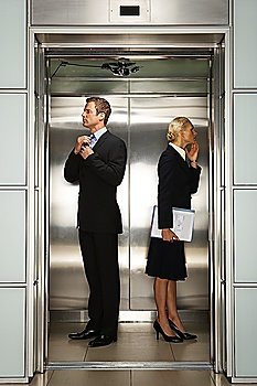 Businessman and Businesswoman checking their reflection in Office Elevator