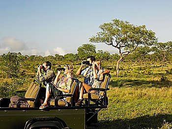 Group of tourists on safari sitting in jeep looking through binoculars