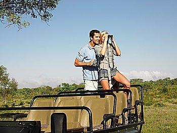 Couple on safari standing in jeep woman looking through binoculars