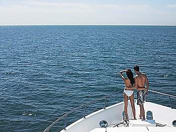 Young couple standing on bow of yacht looking at seascape back view