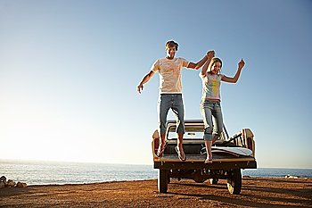 Young couple jumping from back of van parked by ocean
