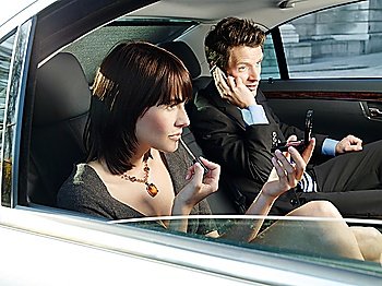 Couple at back seat of car woman applying make-up man using mobile phone