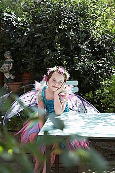 Portrait of young girl (5-6) in fairy costume sitting at garden table