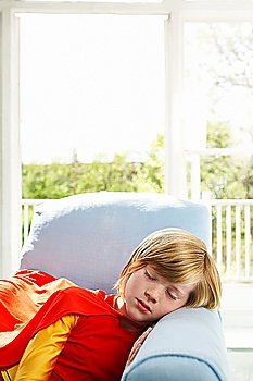 Young boy (7-9) sleeping in armchair wearing superhero costume indoors