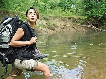 Young woman carrying backpack walking in water looking over shoulder