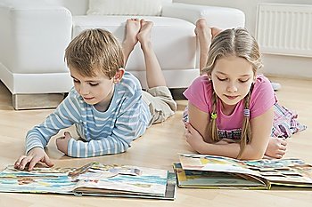 Siblings reading story books on floor in the living room