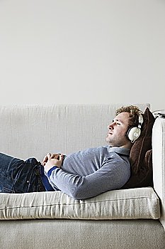 Man wearing headphones lying on sofa in living room  side view