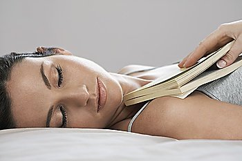Young woman holding book asleep on bed  close-up