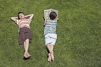 Two boys (6-11) lying on grass  one reading  elevated view