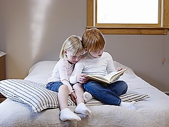 Two sisters sit reading on a single bed