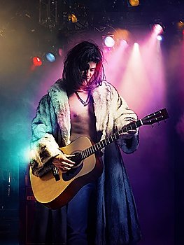Young rock musician in fur coat playing guitar at concert