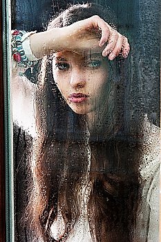 Portrait of a lovely young lady looking through glass window - Indoor in a dark cloudy day  she looks down at left   her head is resting on the right 