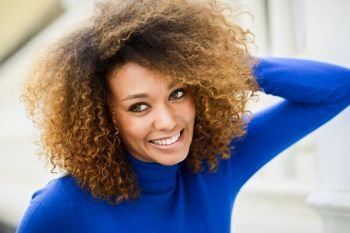 Close-up portrait of beautiful young African American woman  model of fashion  smiling with afro hairstyle and green eyes wearing blue sweater in urba