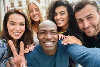 Multiracial group of friends taking selfie in a urban street with a black man in foreground Three young women and two men wearing casual clothes