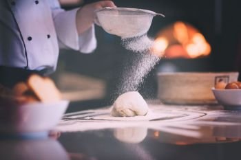 chef sprinkling flour over fresh pizza dough on kitchen table chef sprinkling flour over fresh pizza dough