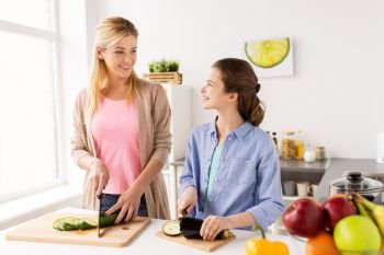 cooking food  family and people concept - happy mother and daughter chopping vegetables for dinner at home kitchen happy family cooking vegetables at