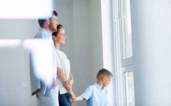 family  people and real estate concept - happy mother  father and little son looking through window at new home or apartment happy family with child 