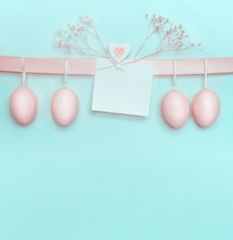 Easter greeting card with pastel pink eggs hanging on ribbon on light  blue turquoise background Creative greeting concept Layout with copy space fo