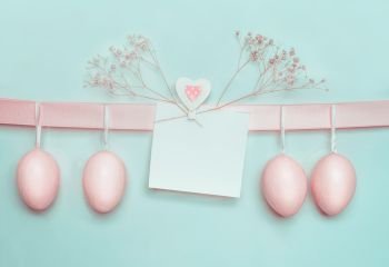 Easter greeting card mock up with pastel pink eggs hanging on ribbon on light  blue turquoise background Creative greeting concept Layout with copy 