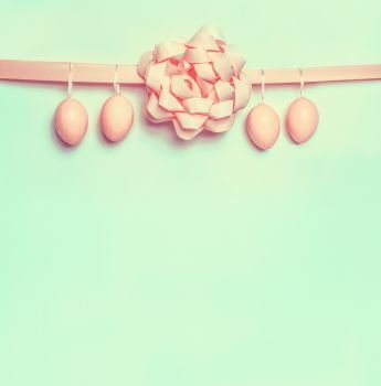 Pastel pink Easter eggs hanging on ribbon with beautiful bow on light green background Creative greeting layout with copy space for your text