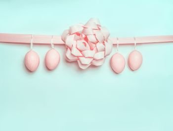 Pastel pink Easter eggs hanging on ribbon with beautiful bow on light  blue turquoise background Creative greeting concept Layout with copy space fo