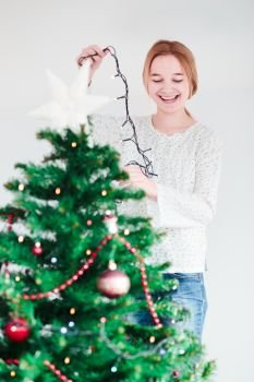 Young girl decorating Christmas tree with lights at home