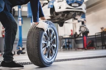 Male mechanic hold and rolling tire at repairing service garage background Technician man replacing winter and summer tyre for safety road trip Tran
