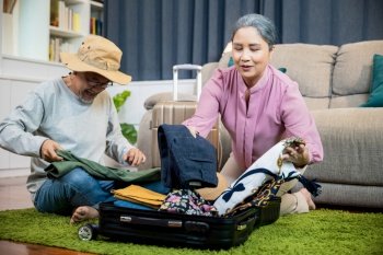 Asian romantic retired couple packing clothes travel bag suitcase together on floor at home interior living room  couple old senior married retired pr