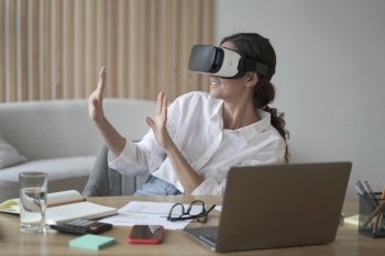 Happy woman exploring augmented world at work  touching 3d virtual objects with hands while sitting at office desk  excited female employee wearing vr