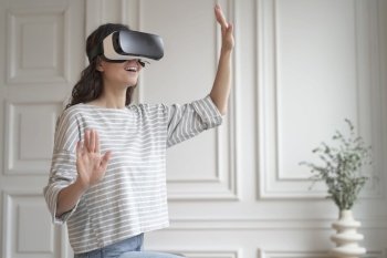 VR In eCommerce Young happy woman in casual clothes standing indoors in virtual reality headset and enjoying fun shopping experience in augmented wor