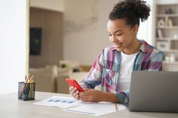Afro teenage girl is distracting while studying remote Teenage girl sitting in front of laptop  clicks mobile phone and chatting African american st