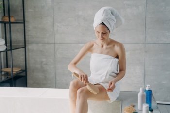 Towel-clad woman massages hip with brush in bathroom Cellulite treatment  body care