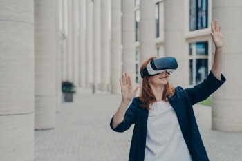Ginger businesswoman in formal attire using VR headset outdoors  exploring virtual world for business purposes