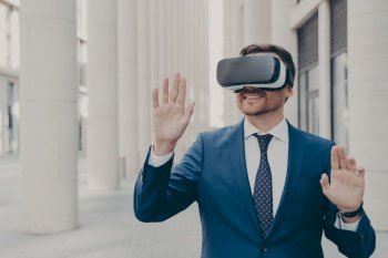 Professional architect in AR headset outdoors  gesturing and smiling  excited businessman using 3D goggles for work  moving virtual objects in air