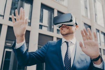 Excited office worker in blue suit outside  using VR glasses to visualize projects  interacting with virtual objects  building in background
