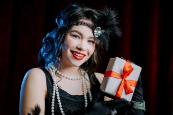 Joyful vintage styled woman dressed in Art Deco era holding gift box with bow on velours background She is glad to get present retro  party  fashion