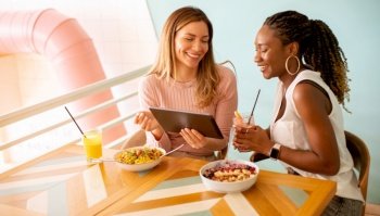 Two pretty young black and caucasian woman having good time  drinking fresh juices and having healthy breakfast in the cafe