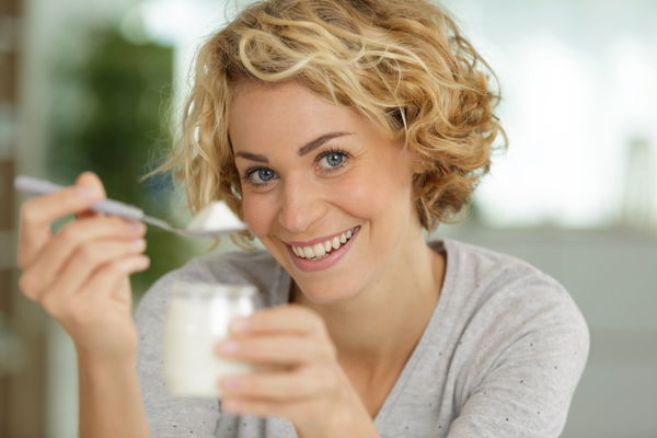 happy young woman eating yogurt in kitchen