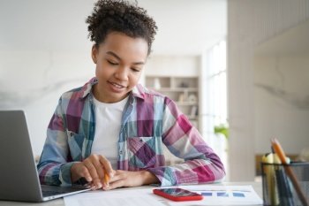 Handsome afro schoolgirl is studying remote at home and doing homework Teenage girl is sitting at the desk in front of computer having online exam R