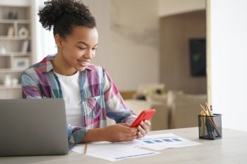 Afro teenage girl is distracting while studying remote Teenage girl sitting in front of laptop  clicks mobile phone and chatting African american st